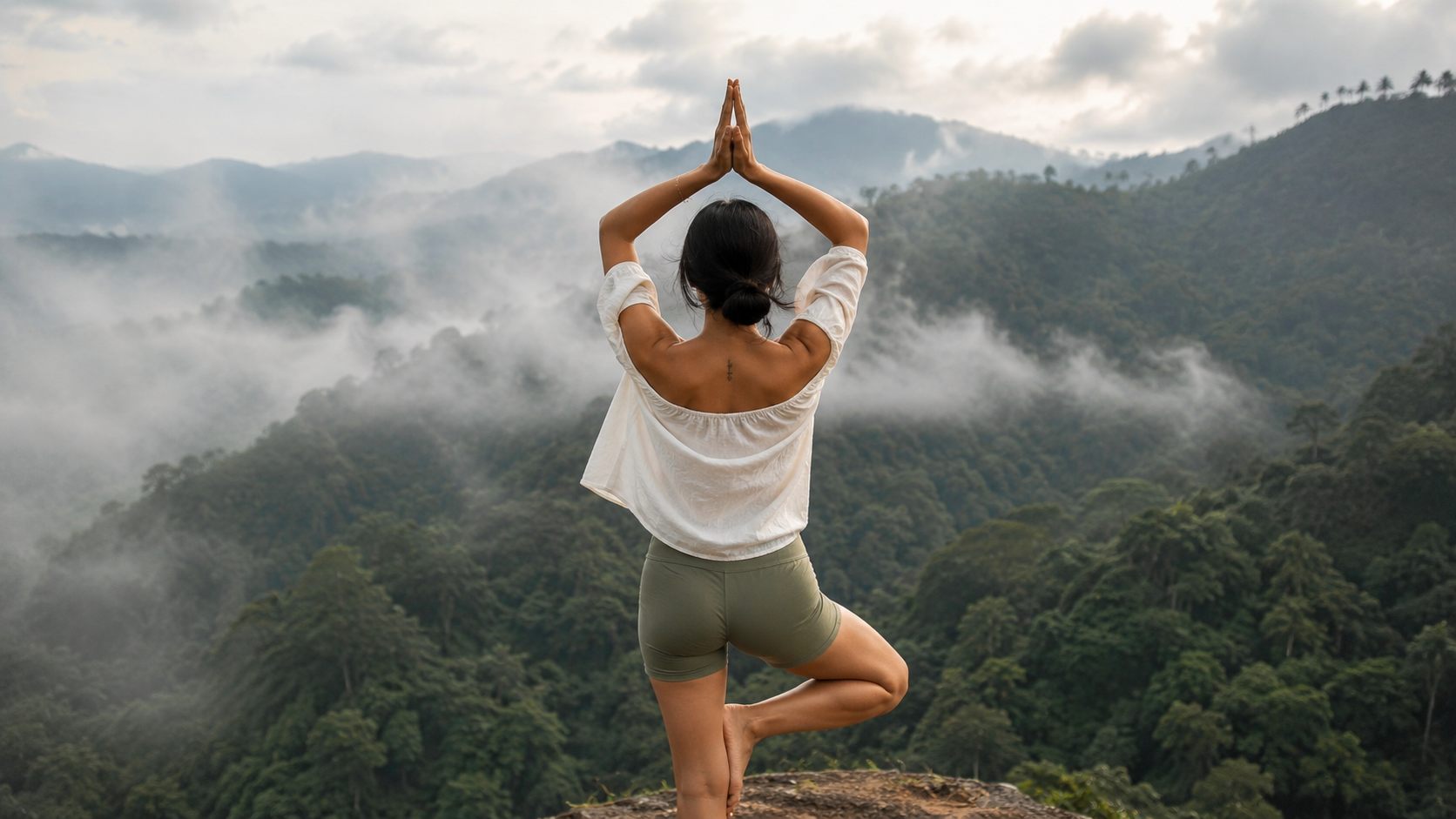 Mila Tan in tree pose overlooking misty mountains at dawn